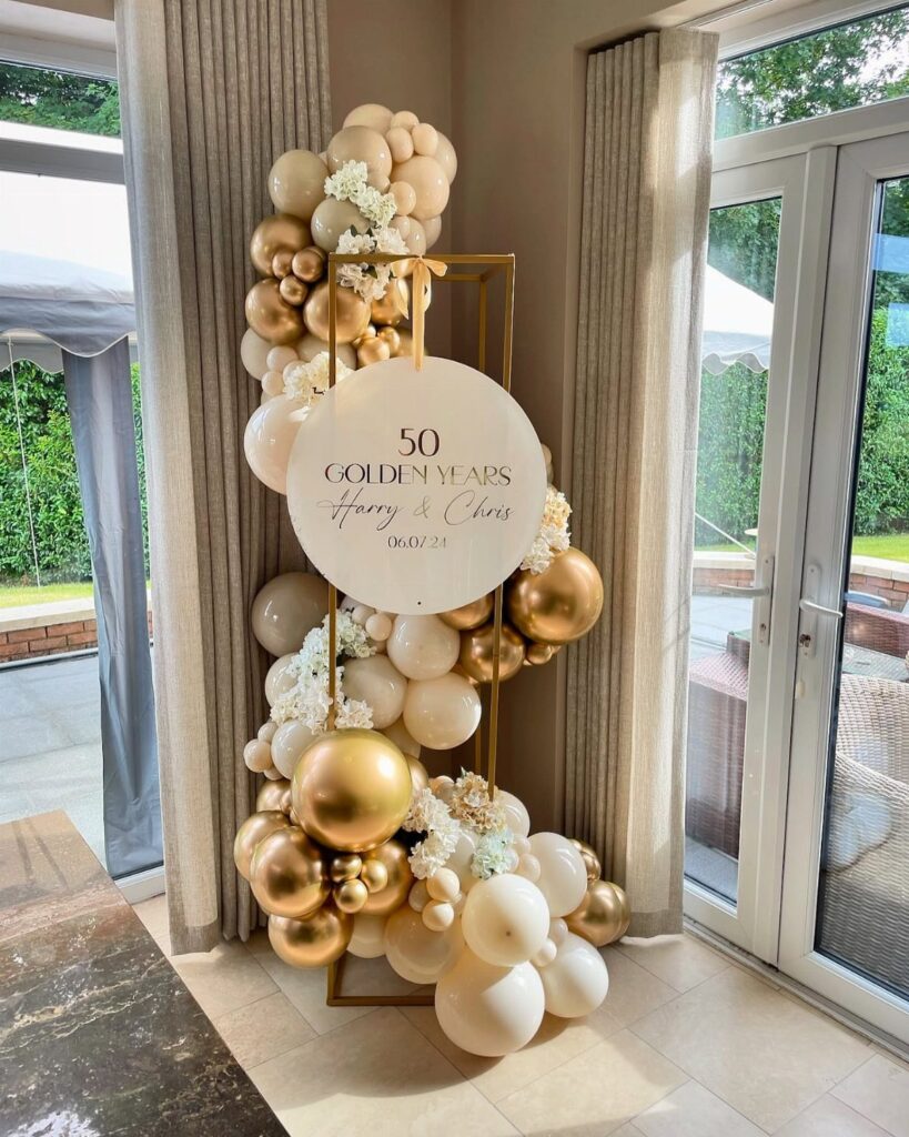 Gold and cream balloon arch with a 50th anniversary sign in a room.