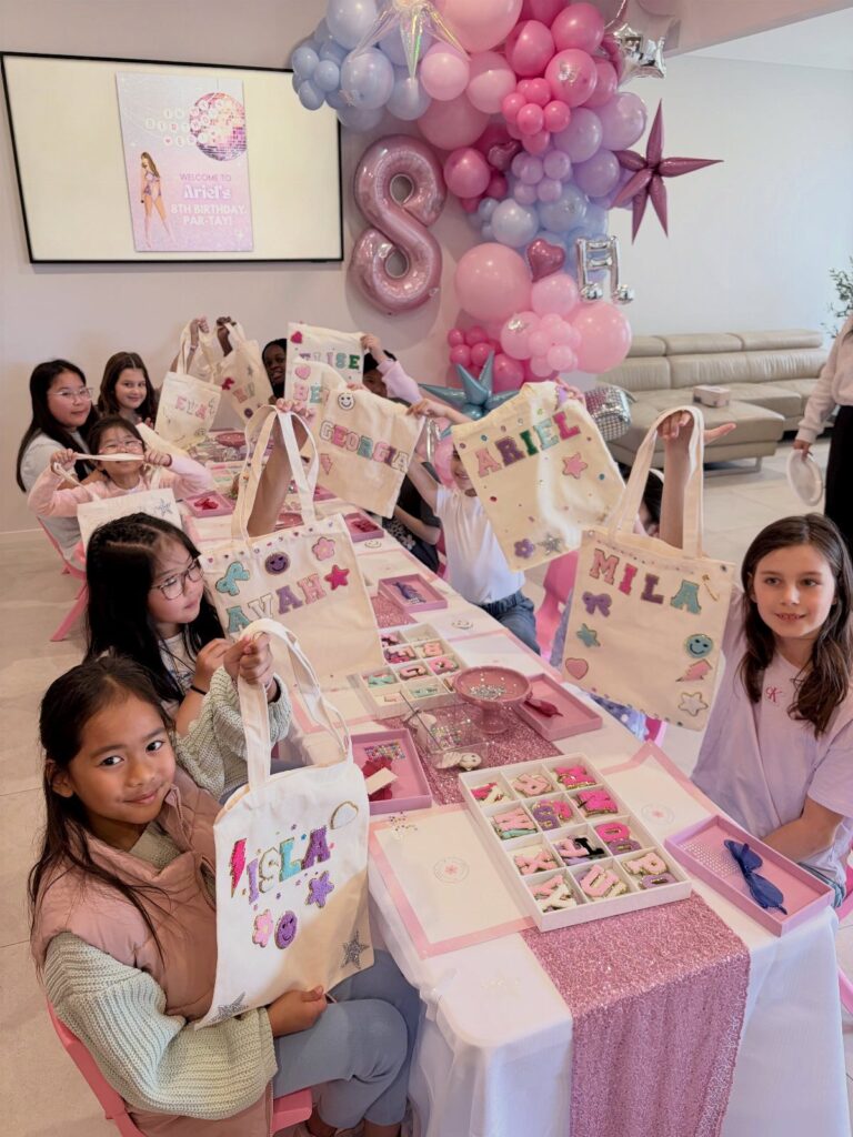 Young girls holding decorated canvas tote bags at a pink themed birthday party.