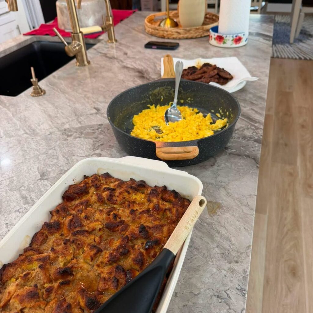 Baked breakfast casserole in a white dish with scrambled eggs and sausage nearby.