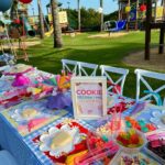 Cookie decorating station table with plain cookies and colorful toppings outdoors near a playground