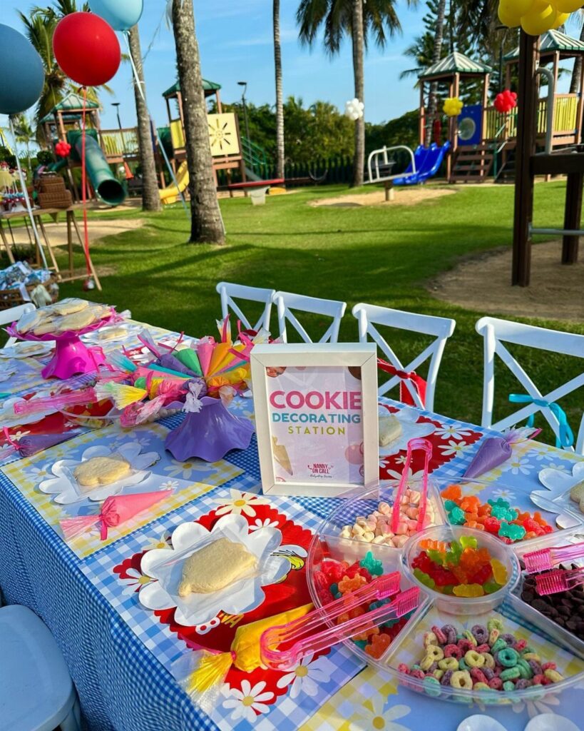 Cookie decorating station table with plain cookies and colorful toppings outdoors near a playground