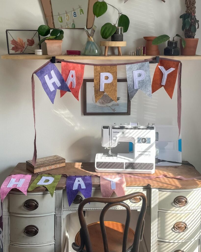 Handmade fabric birthday banner spelling HAPPY BDAY in a sewing room workspace