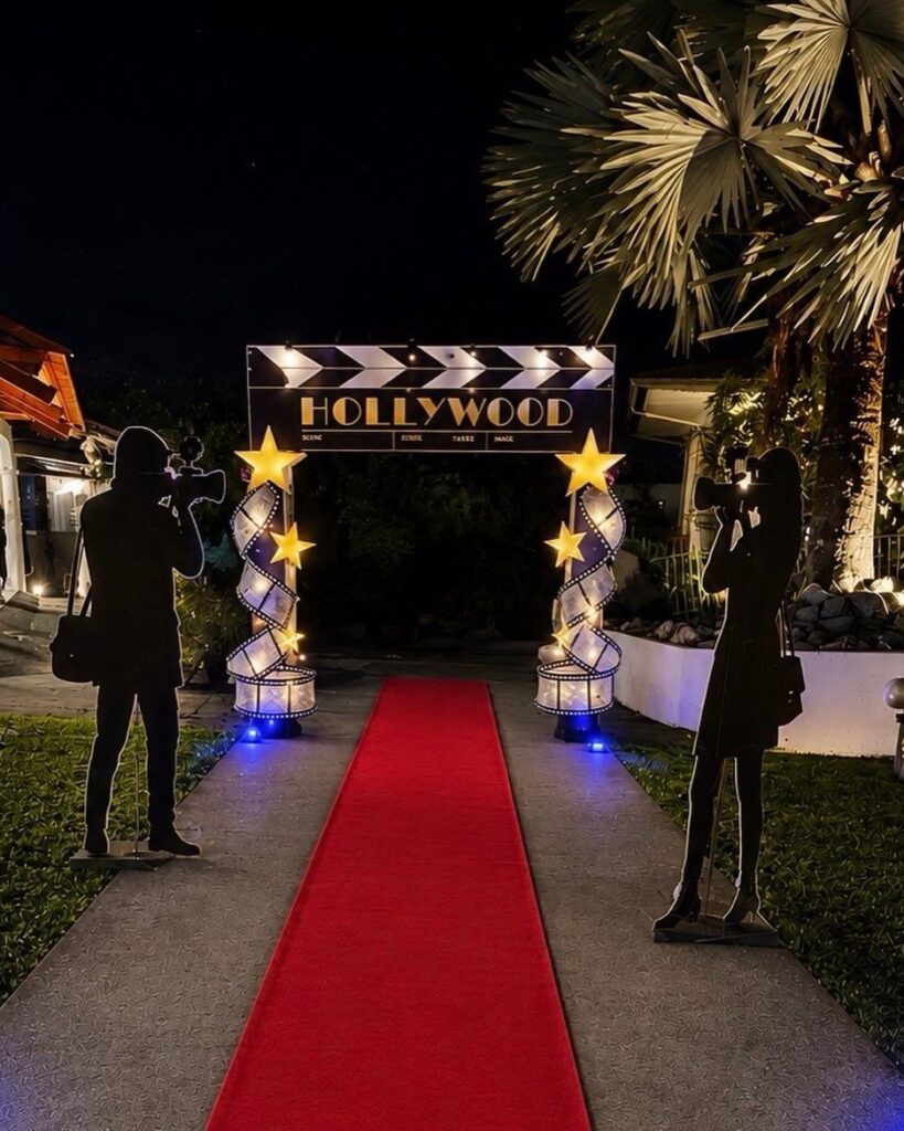 Red carpet entrance with Hollywood clapperboard sign and photographer silhouettes at night.