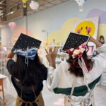 Two decorated graduation caps, one with an ocean wave and one with flowers.