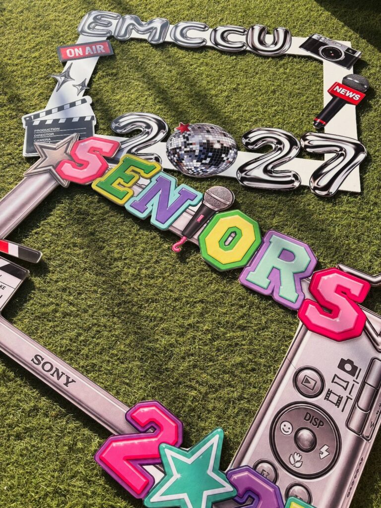 Decorative cardboard photo frame for seniors class of 2027 resting on green grass.