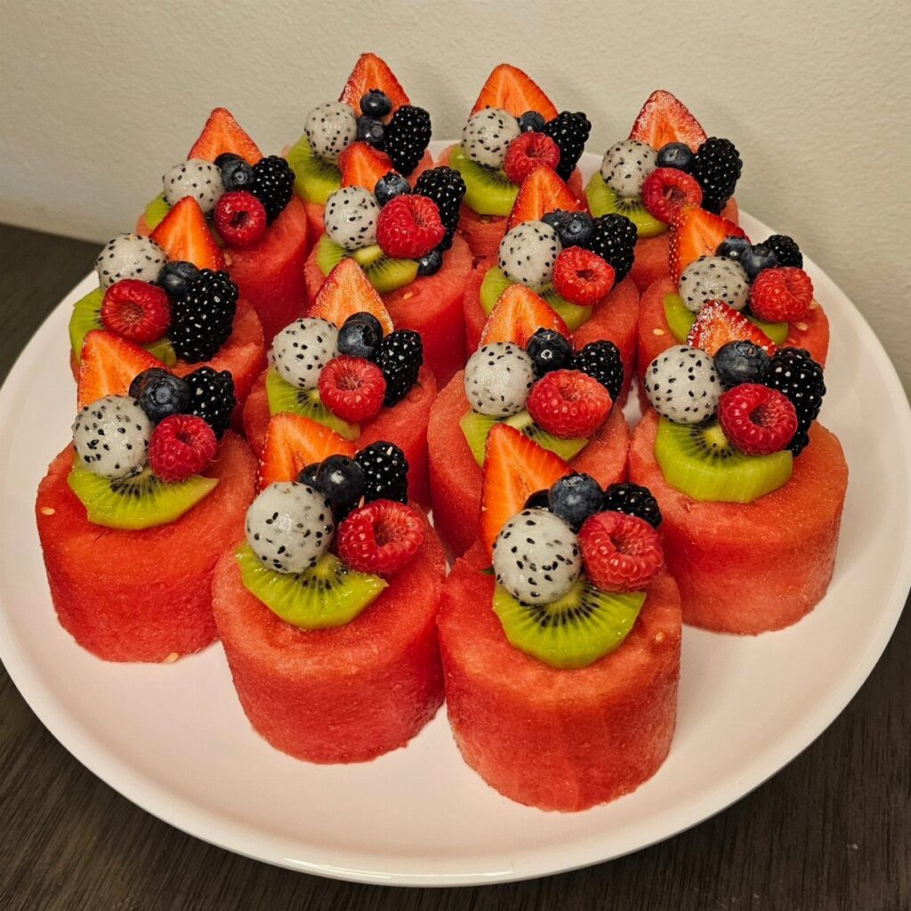 Watermelon cylinders topped with assorted fresh berries, kiwi, and dragon fruit on a plate.