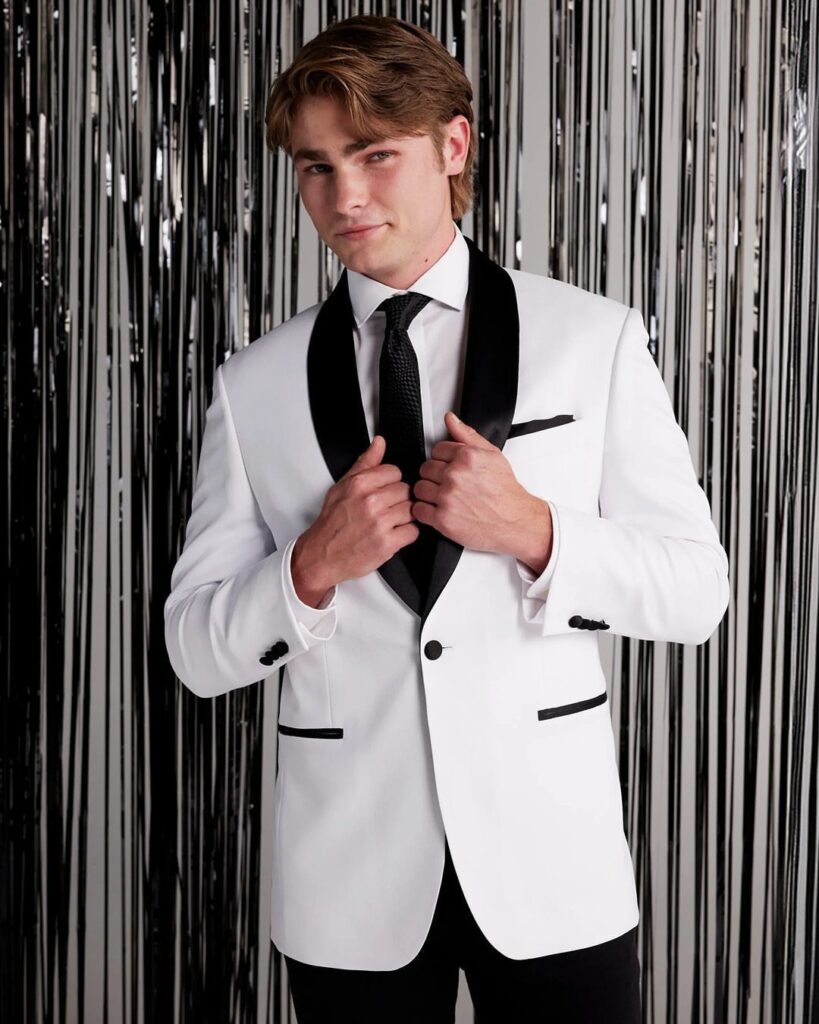 Young man in a white tuxedo with black lapels posing against silver tinsel.