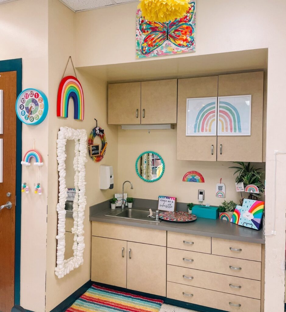 Classroom corner with rainbow decorations, light wood cabinets, and a colorful striped rug.