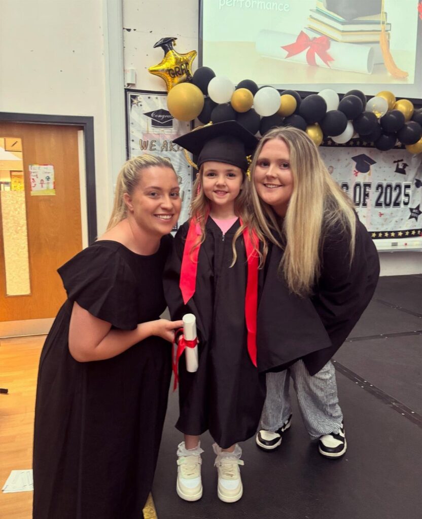 Young girl in graduation cap and gown posing with two adults at ceremony