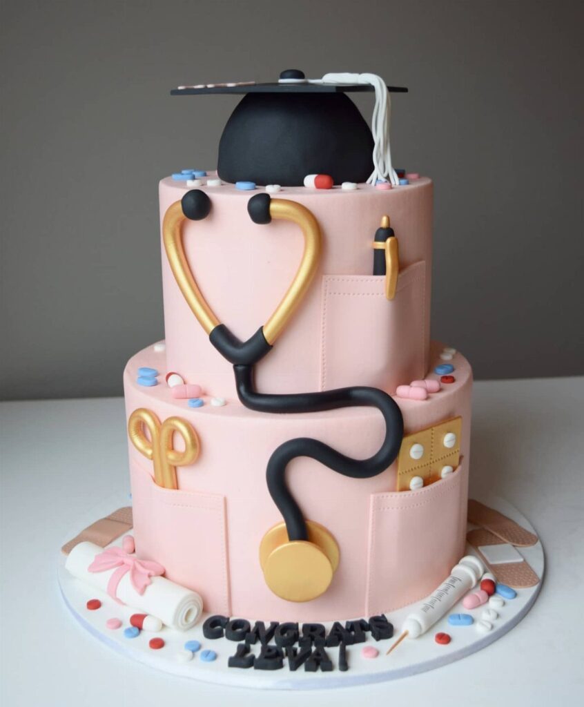 Two-tier pink nursing graduation cake with a graduation cap and medical tools.
