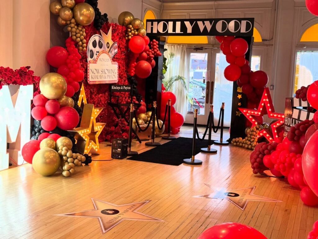 Hollywood themed event decor with red and gold balloons, black carpet, and stars.