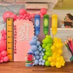 Graduation backdrop with colorful balloons, giant crayons, a ruler, and 2024 signage.