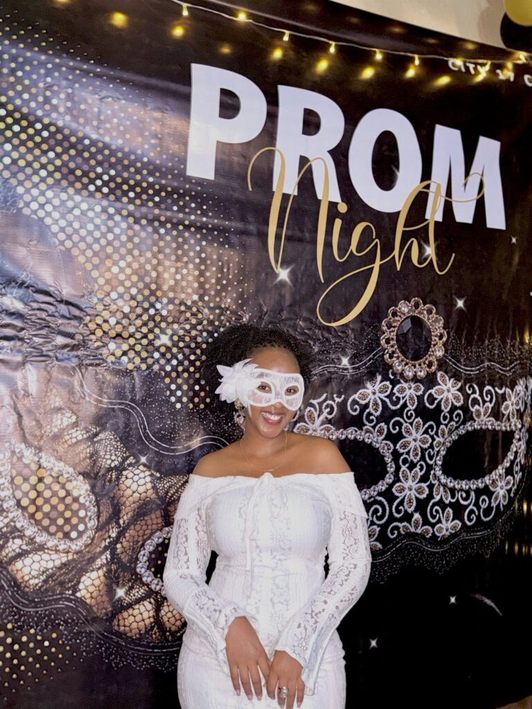 Woman in white lace dress and masquerade mask posing before prom backdrop