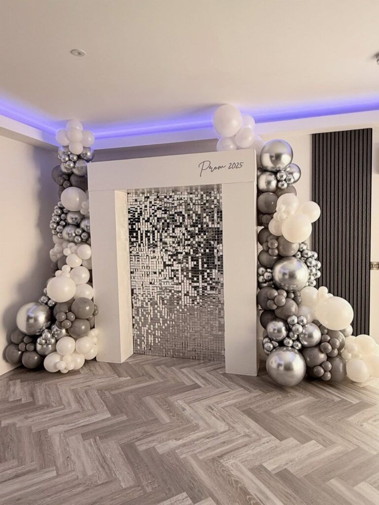 Prom photo booth with white and silver balloon arches and sequin backdrop