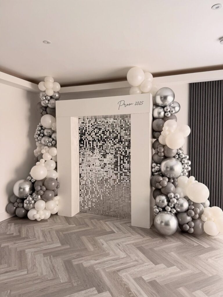 White archway with silver and white balloons and a shimmering tinsel backdrop.
