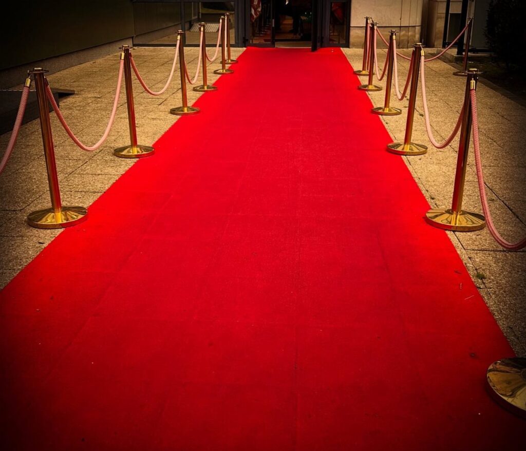 Red carpet leading to an entrance with gold stanchions and red velvet ropes.
