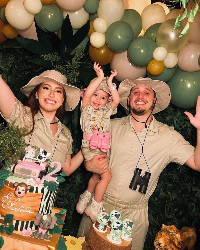 Family in khaki safari outfits posing by a balloon arch and themed cake.