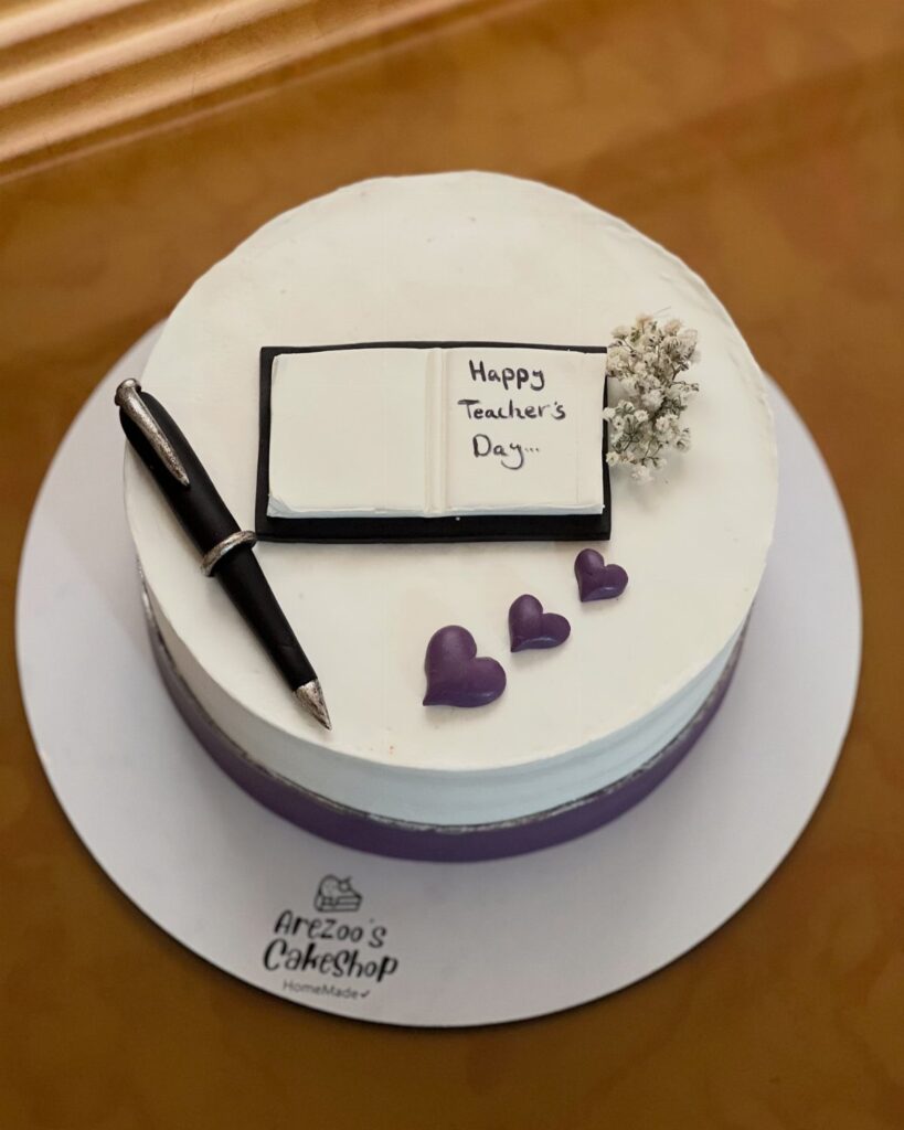 White frosted cake decorated with a fondant book, pen, and purple hearts.