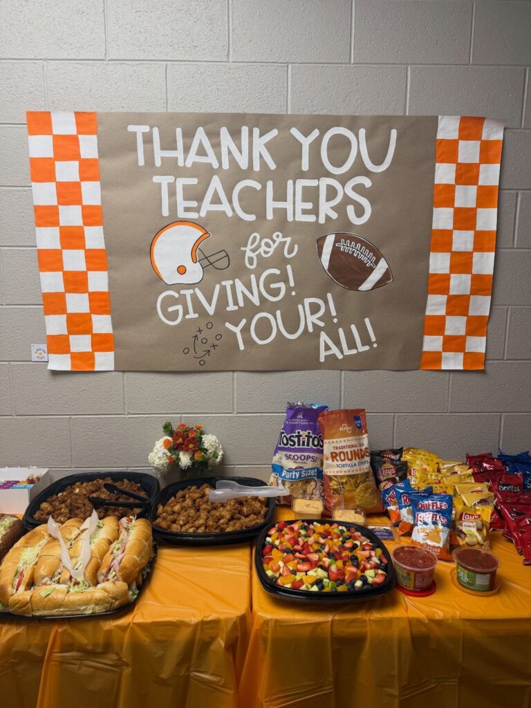 Catered meal spread with sandwiches and snacks under a thank you teachers banner.