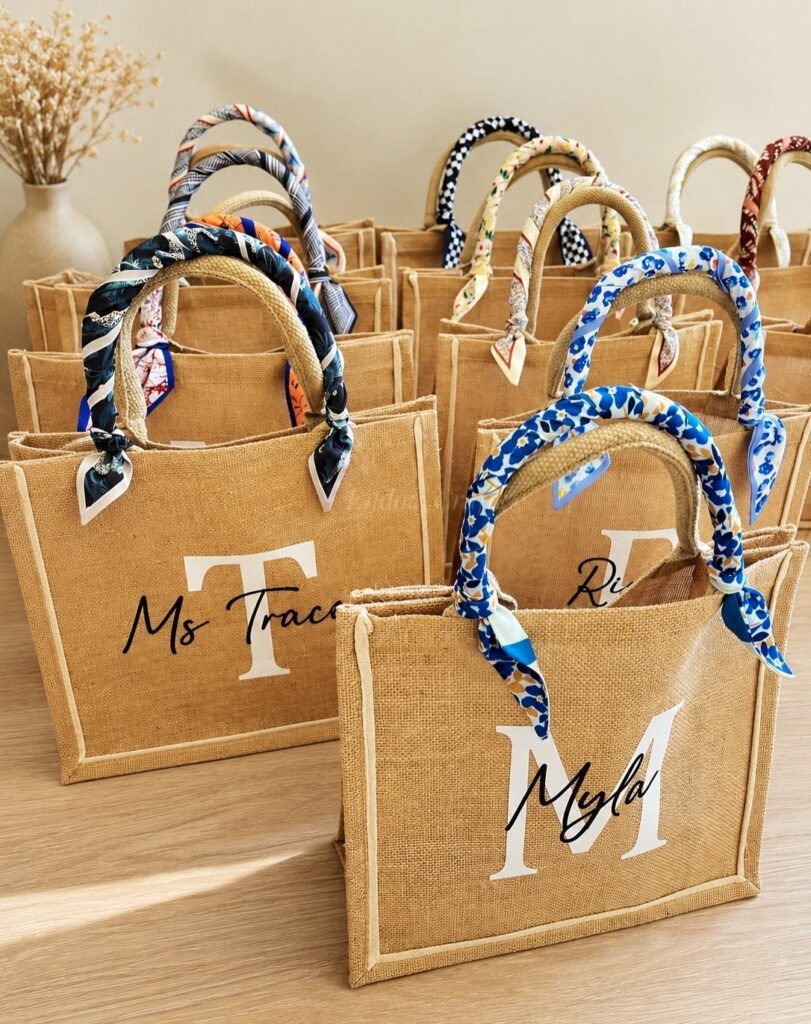 Personalized jute tote bags with colorful scarf handles and white printed names.