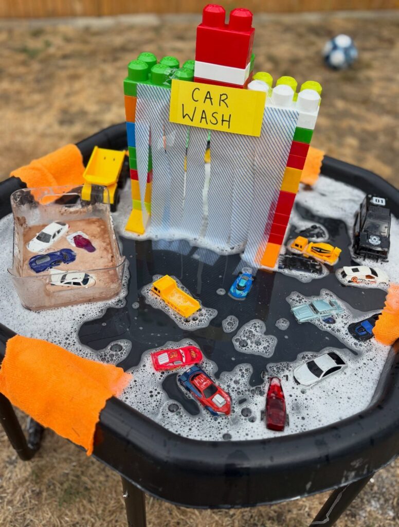 Toy car wash setup with soapy water, colorful blocks, and a handwritten sign.